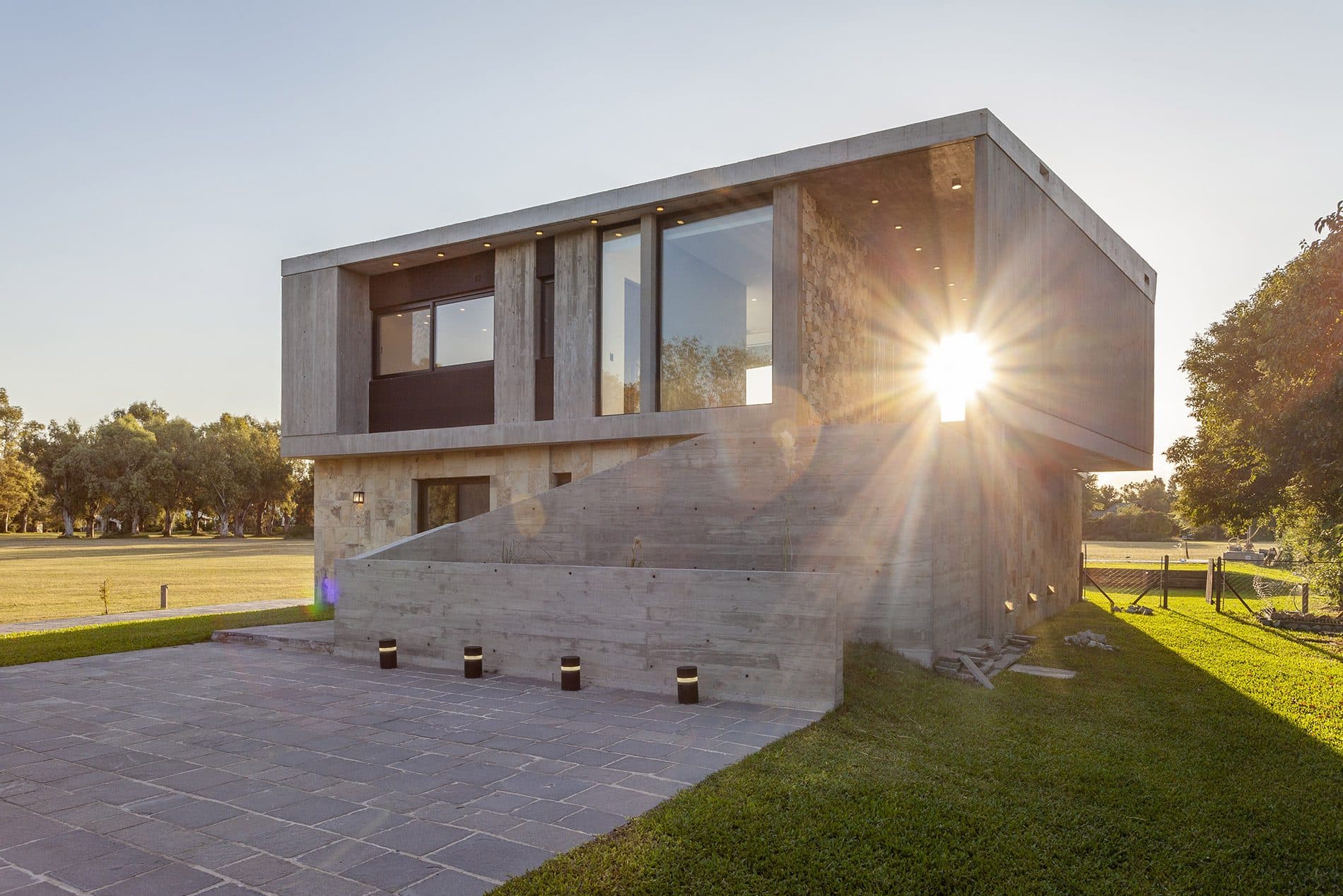 Casa de hormigón y piedra al atardecer, con el sol entre sus volúmenes
