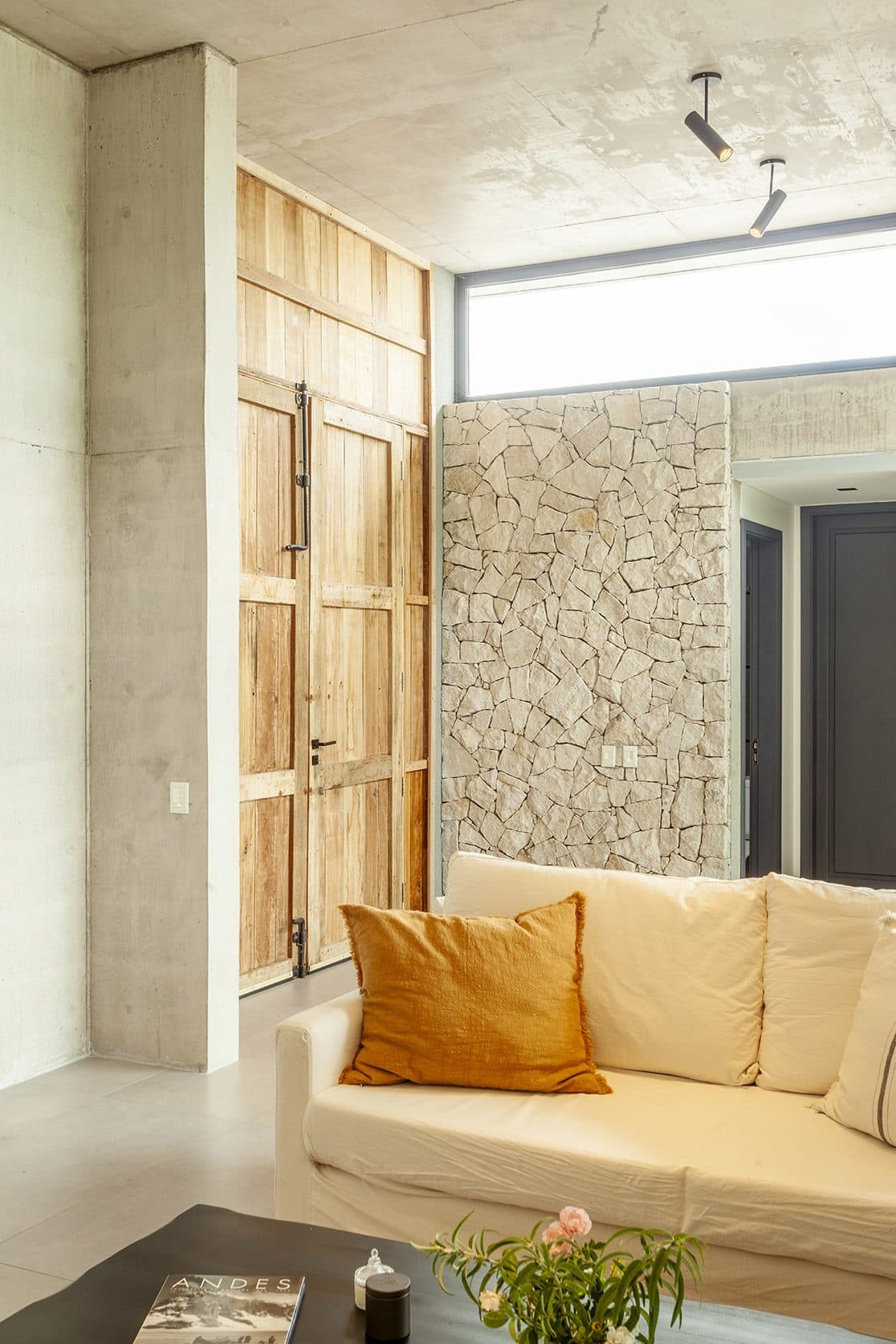 Interior con pared de piedra, carpintería de madera y sillón claro